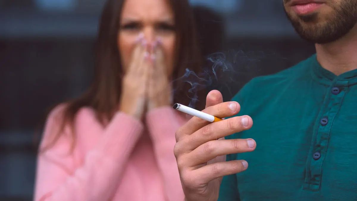 A person inhaling secondhand smoke, illustrating the dangers of passive smoking